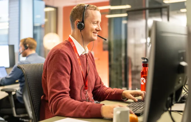 Circle K employee happily helping a customer on a call, wearing a headset at his desk