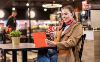 Woman happily using her tablet in a Circle K café, with her coffee in hand